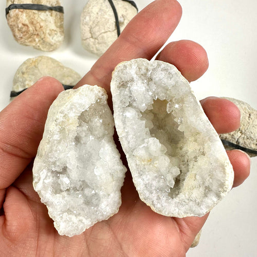 Hånd holder to halvdele af en kvarts geode med skinnende krystaller indeni.
