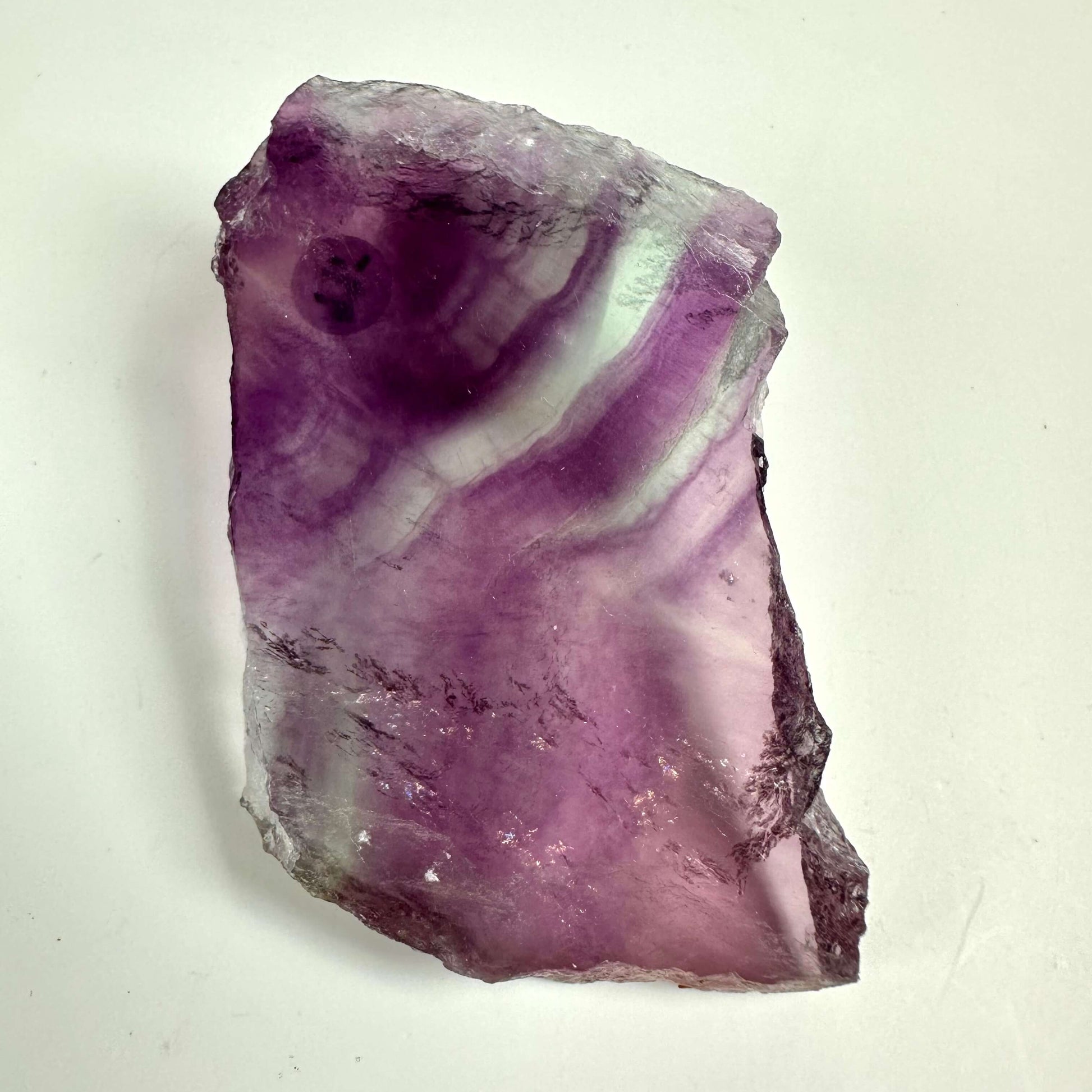 Regnbue fluorit skive i nuancer af lilla og hvid på en hvid baggrund.