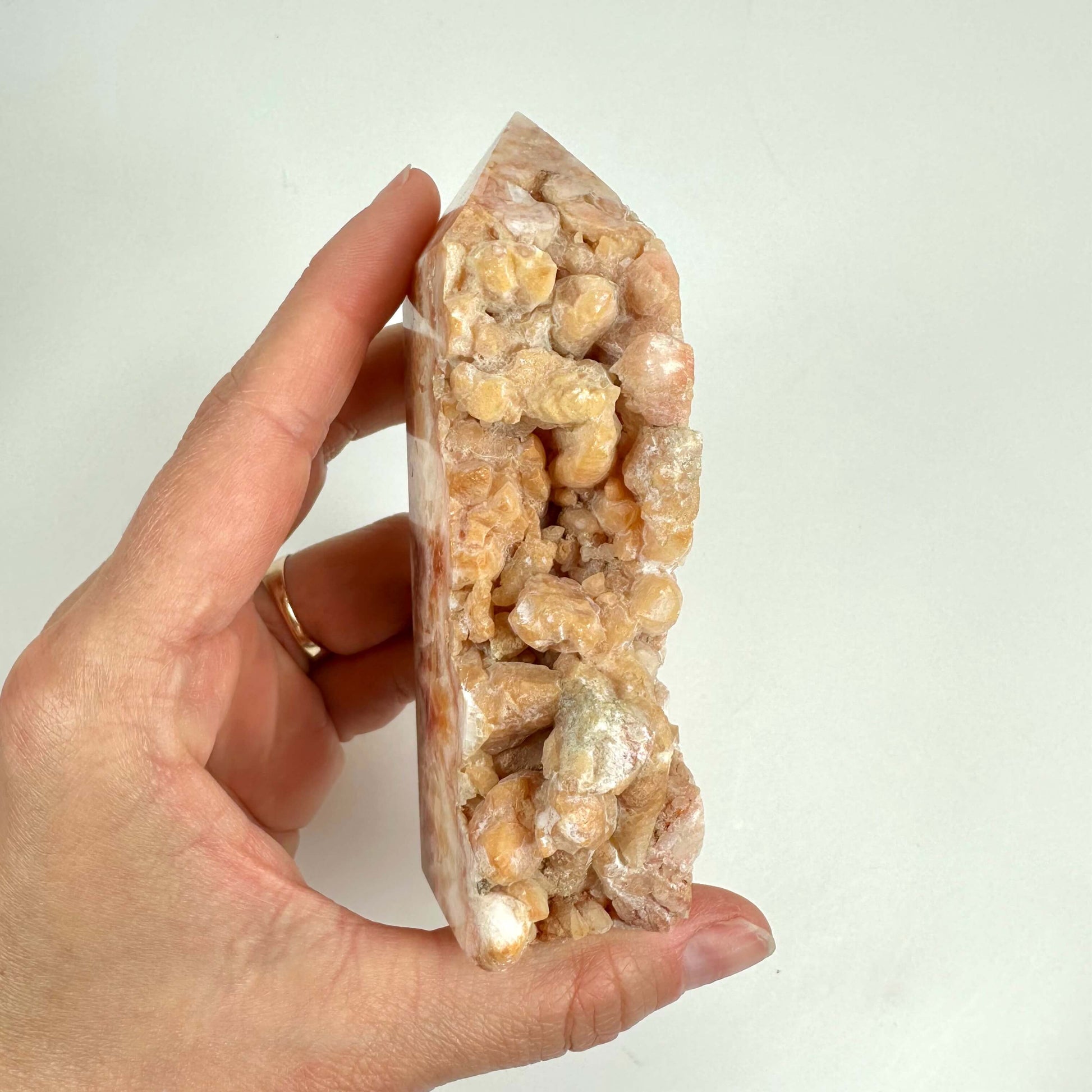 En hånd holder en spids krystalformet Calcit hundetand med beige og lyserøde nuancer.