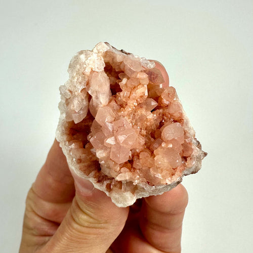 En pink ametyst geode holdes i hånden, viser sine rosa krystaller mod en hvid baggrund.