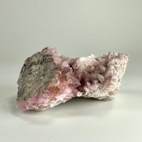 Klynge af rosa Cobalto calcit krystaller på en grå stenmåtte, fotograferet mod en lys baggrund.