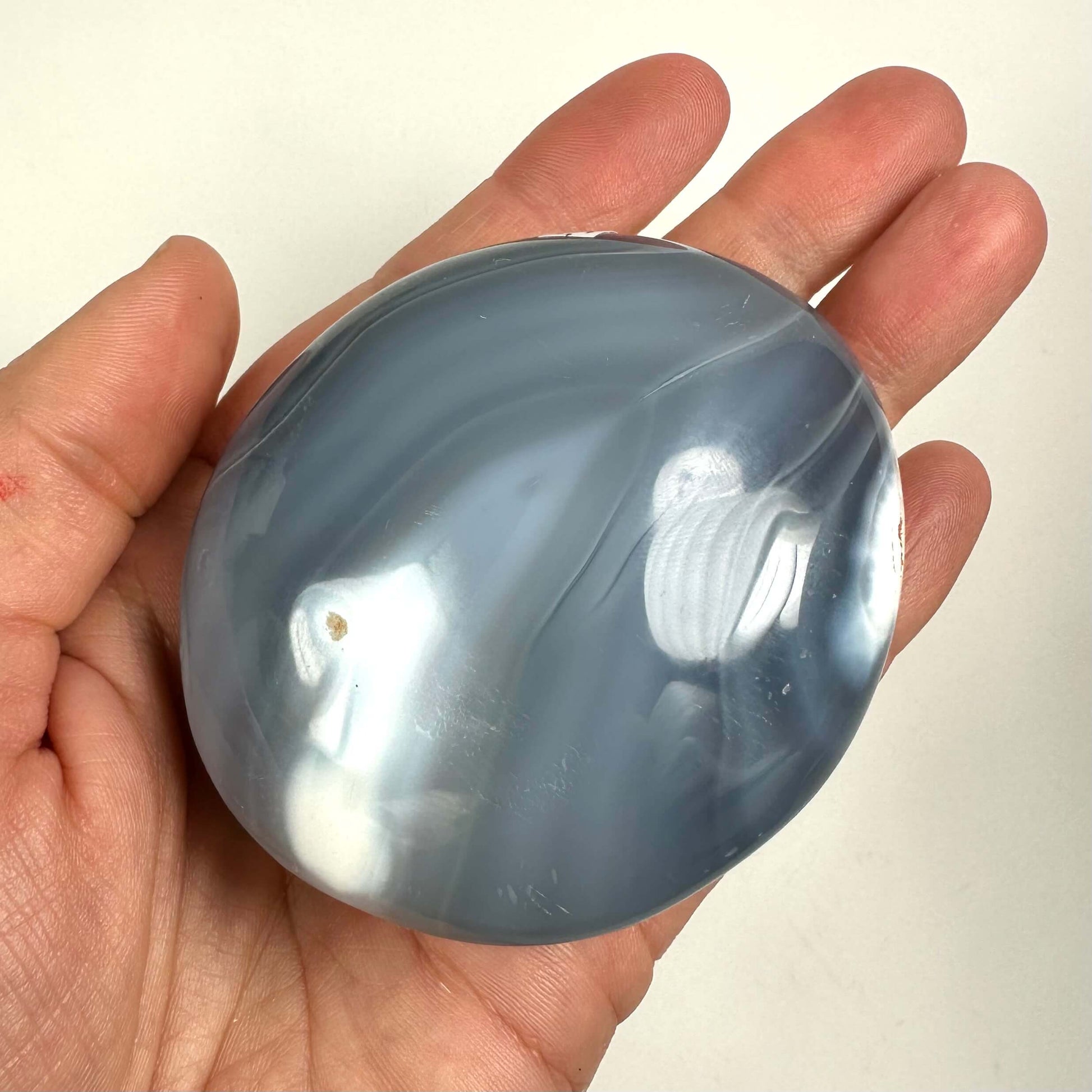 Hånd holder en glat orca agat palmstone med blå og hvide nuancer.