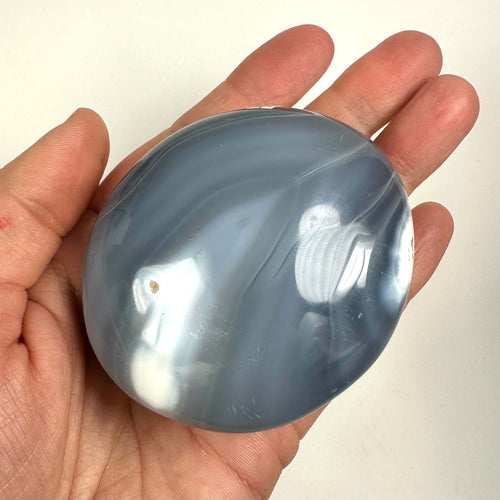 Hånd holder en glat orca agat palmstone med blå og hvide nuancer.