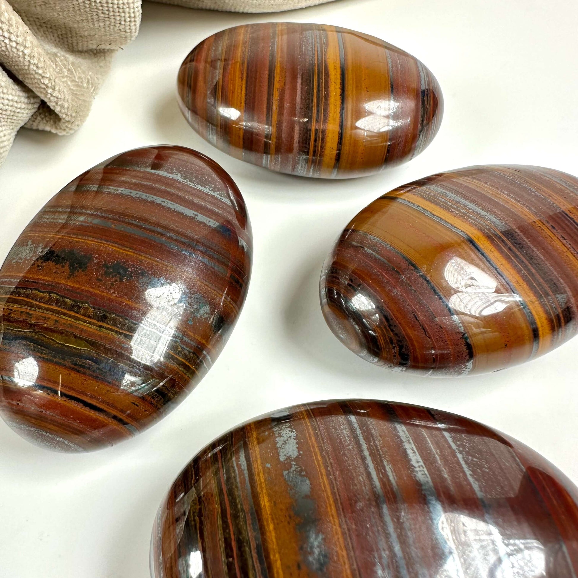 Fire glatte Okse- og tigerøje palmstones vises på en hvid overflade ved siden af et stof.