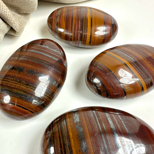 Fire glatte Okse- og tigerøje palmstones vises på en hvid overflade ved siden af et stof.