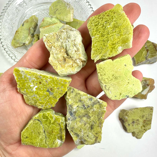 Hånden holder flere grønne mineralsten på en tallerken.