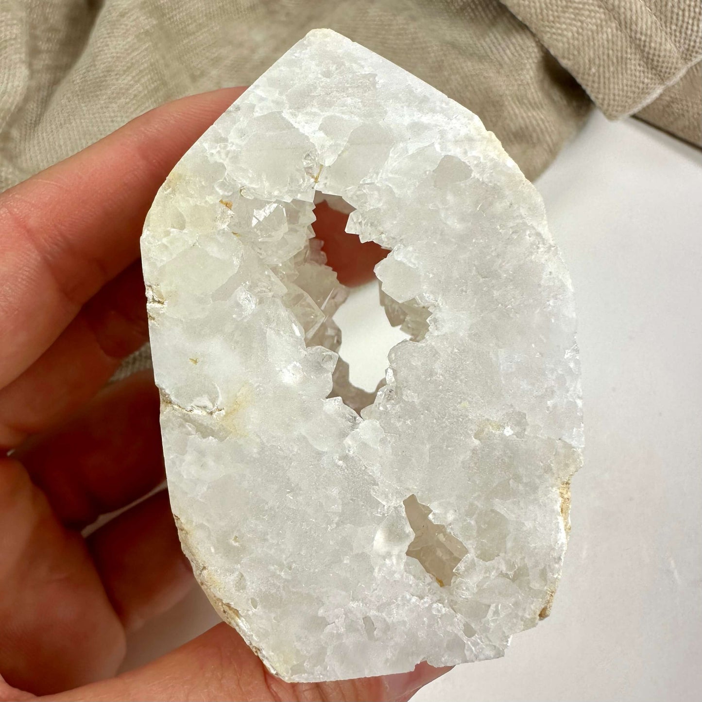 En hånd holder en kvarts geode tårn med en krystalhule i midten.