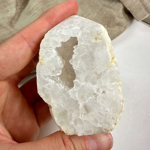 Hånd, der holder en kvarts geode tårn med krystalstruktur mod en neutral baggrund.