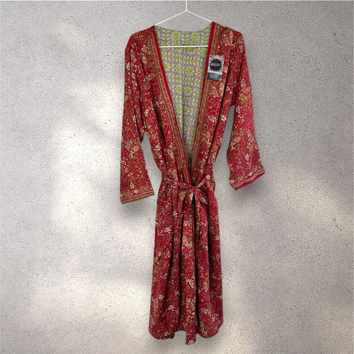 Rød kimono med blomsterprint hænger på bøjle foran en grå væg.