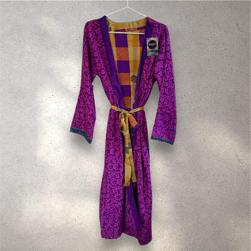 Lilla kimono med blomstermønster og gult bælte hænger på en grå væg.