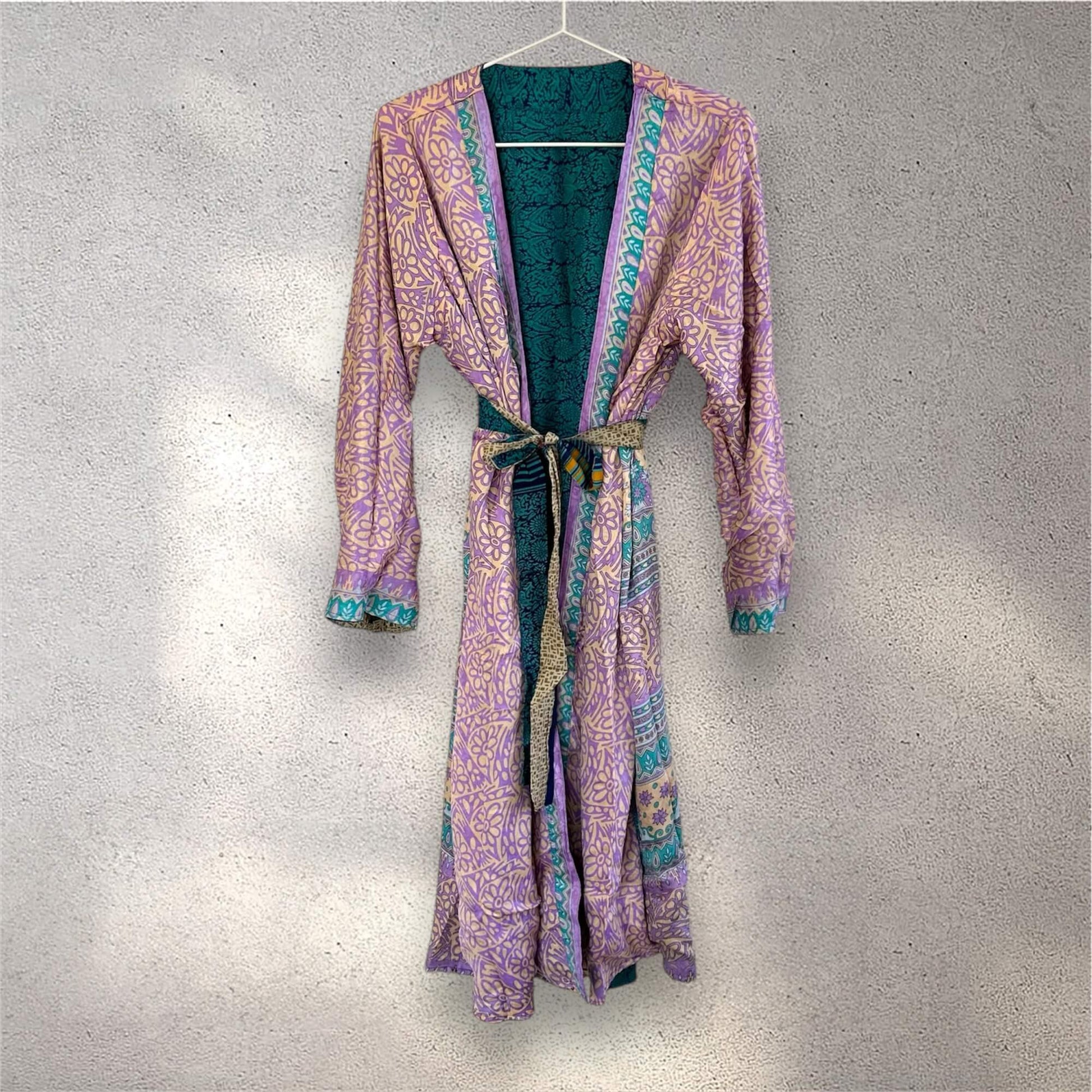 Lilla og grøn mønstret kimono hænger på en bøjle mod en grå væg.