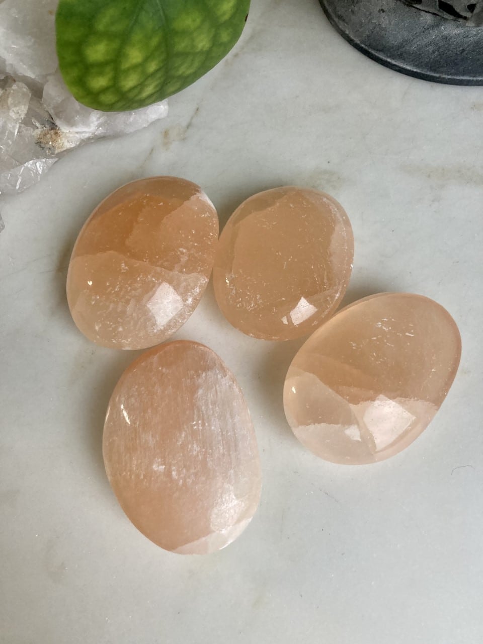 Fire ovale alabaststen på en lys overflade med et grønt blad i baggrunden.